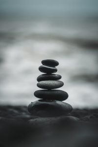 6 stones, precariously balanced on each other on the beach, with the ocean - fuzzy and out of focus - behind it.