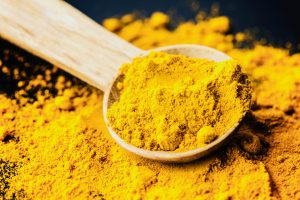 A pile of golden powdered turmeric with a wooden spoon in it, ready to use, for flavor and  anti-inflammatory properties
