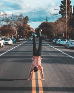 a fella in a red and white striped shirt and black jeans doing a handstand on the double yellow line in the middle of a blacktop road. Oh, and he's wearing teal argyle socks. 