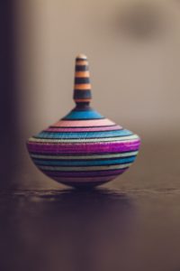 A picture of a spinning top, made out of different layers of dyed wood and shaped on a lathe. At least 33 by my count, of aqua, blue, lime green, fuschia, pale pink, peach, black, and brown. Kinda makes me want a top. 