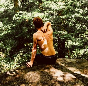 Shirtless rock climber trying to rub his own back